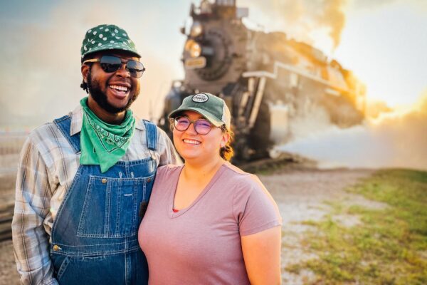 A smiling couple standing next to a historic steam locomotive.